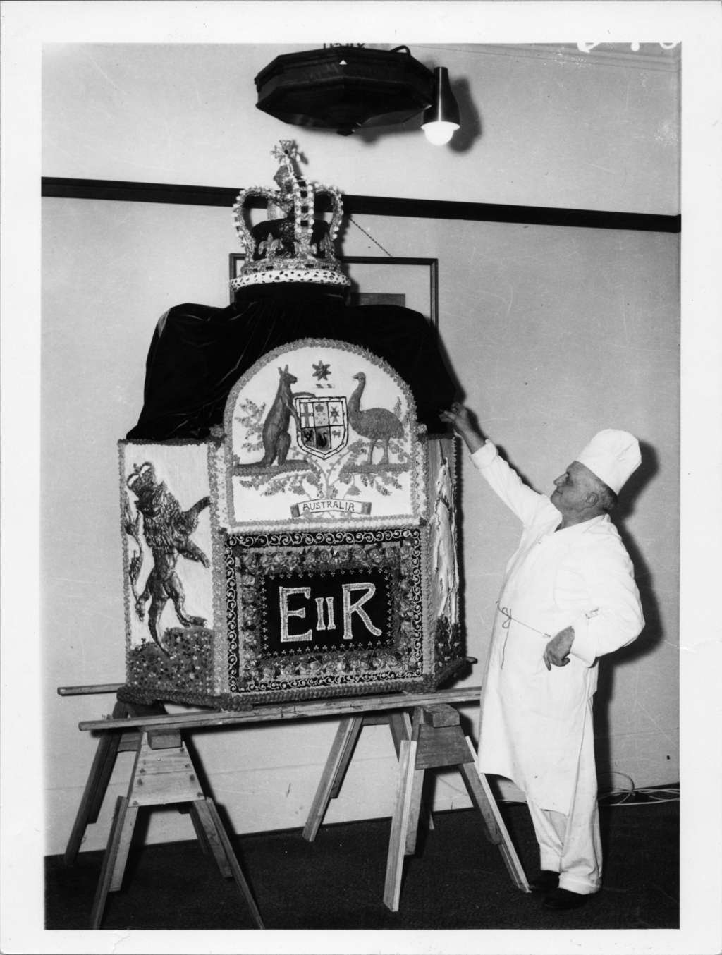 A man presents an ornate sculpture depicting the Australian coat of arms above the letters EIIR, flanked by a lion and unicorn and topped with a jewelled crown.