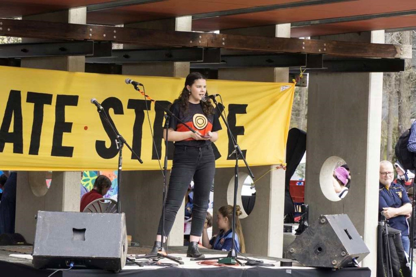 Dhani Gilbert speaks into a microphone, on stage, for a school strike for climate change protest