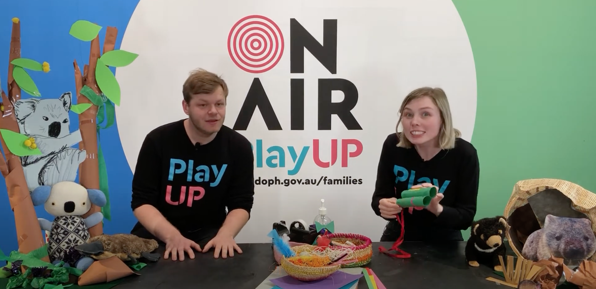 Two PlayUP facilitators stand behind a table with lots of craft supplies. 