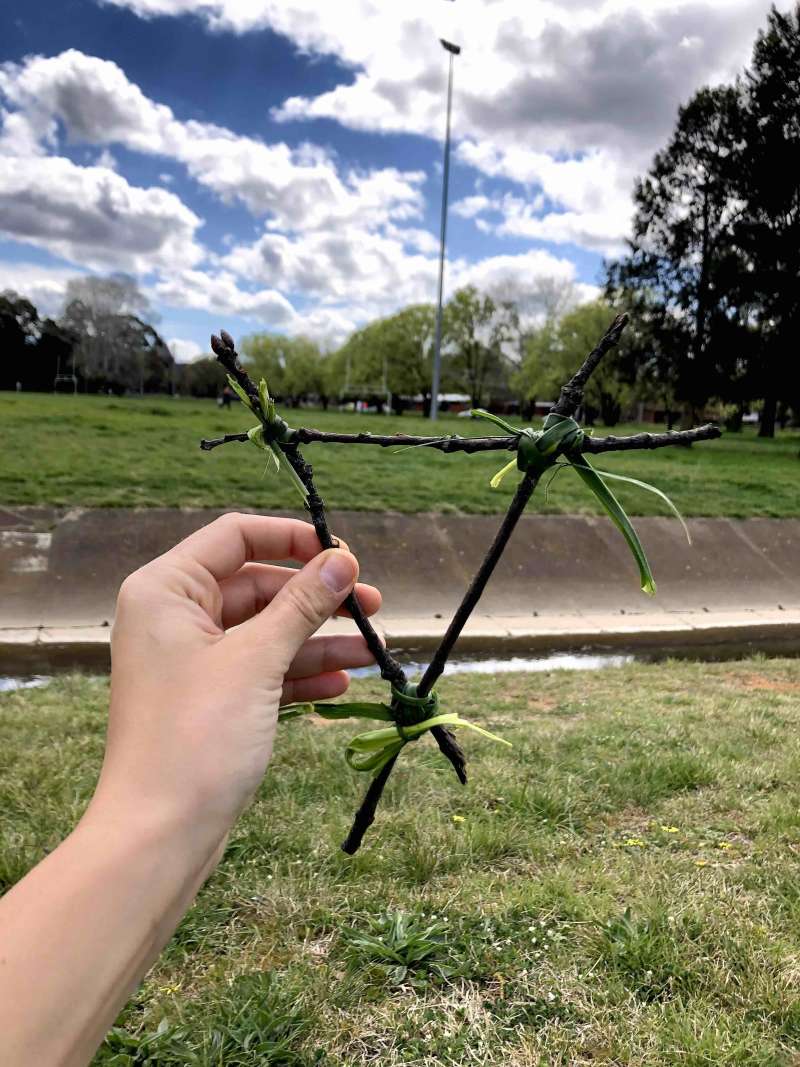 A close up of 4 sticks in the shape of a triangle held together by grass in the corners. 