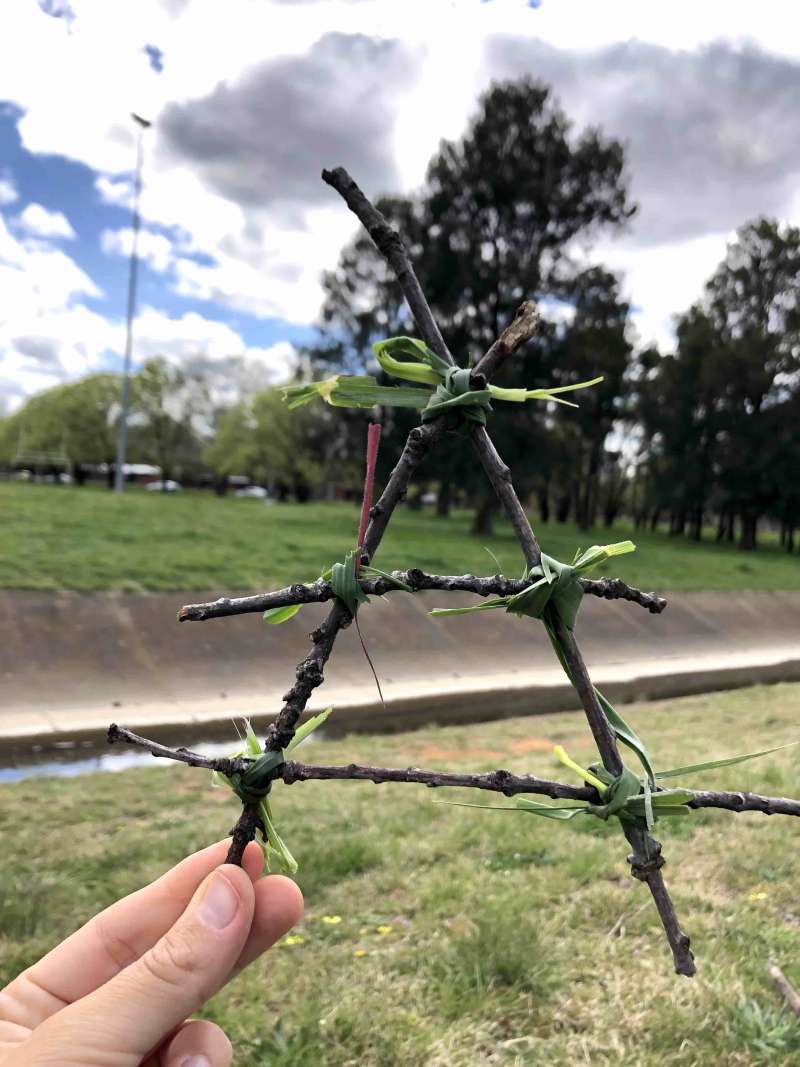 A close up of 4 sticks that look like a triangle held together by grass. It is the size of a hand. 