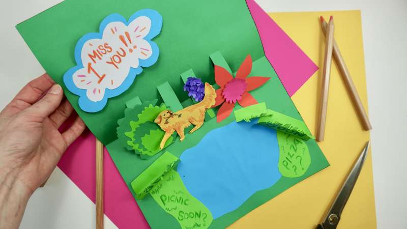 A colourful handmade card that features a lion in a forest next to a lake and the words 'I miss you'.