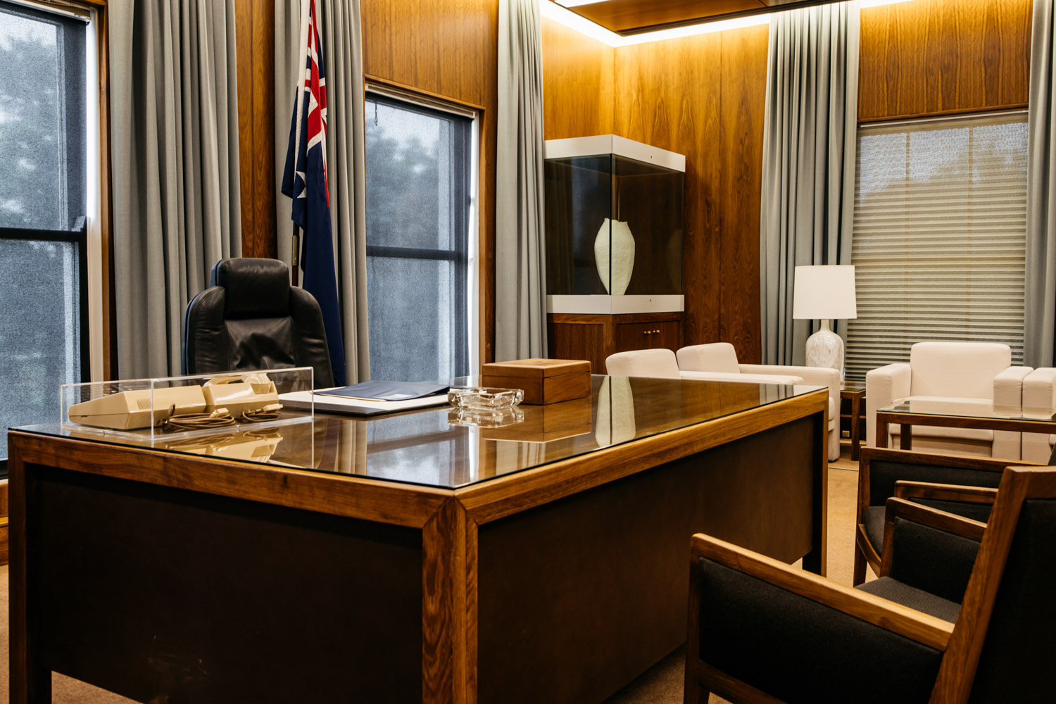 A colour photograph of the Prime Minister's Desk. Behind it is a comfortable office chair and an Australian flag on a pole. In front and to the side of the desk are armchairs. A colour photograph of the Prime Minister's Desk. Behind it is a comfortable office chair and an Australian flag on a pole. In front and to the side of the desk are armchairs.