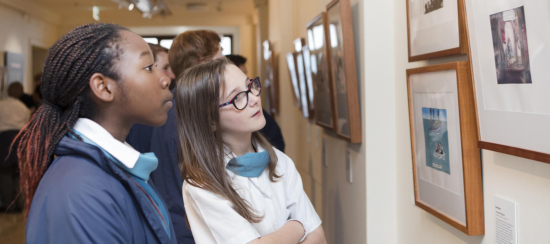 Two school children looking at the artwork in Behind the Lines Two school children looking at the artwork in Behind the Lines