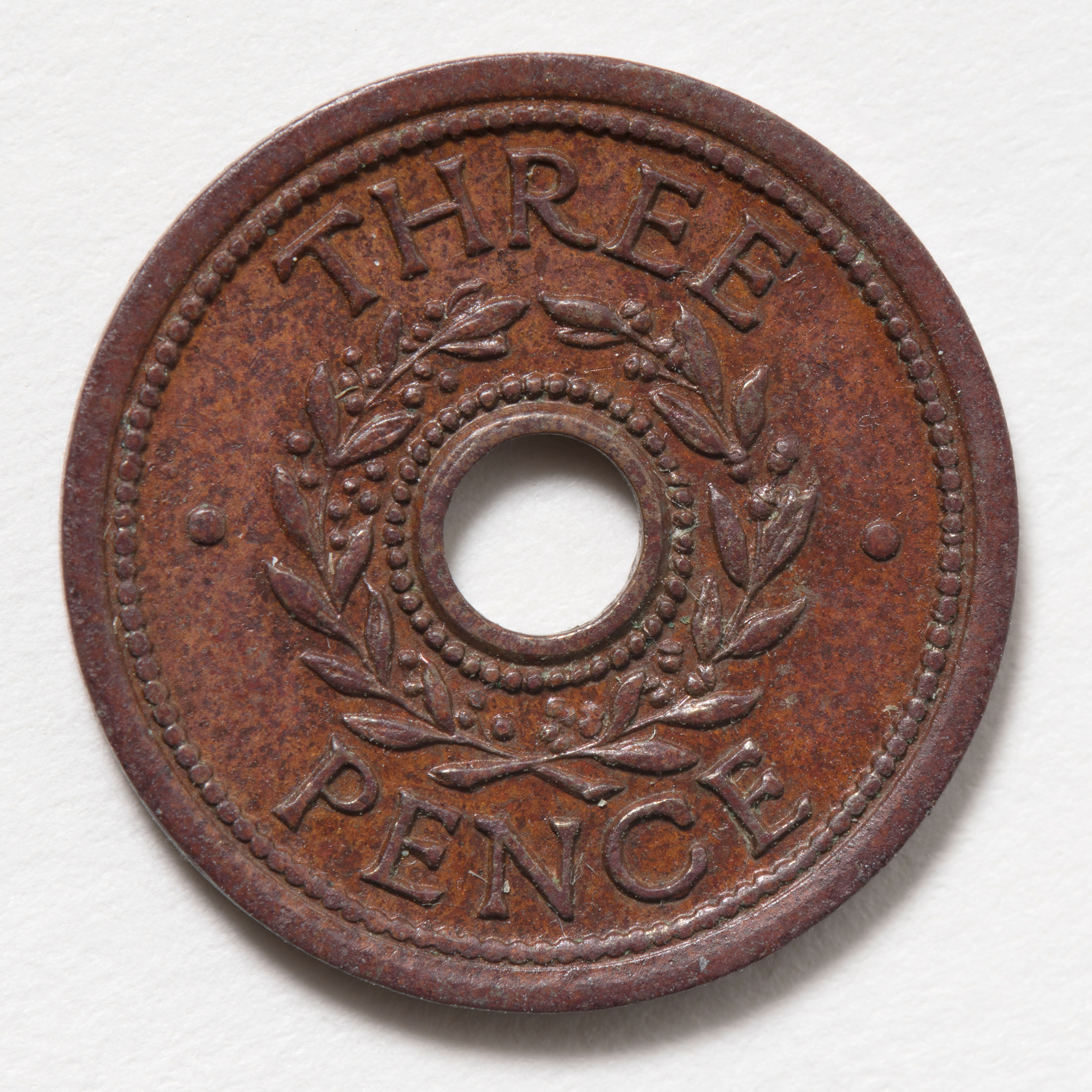 A brown old coin with the words three pence on the front. There is a hole in the middle of the coin with a wreath that goes around the hole. 