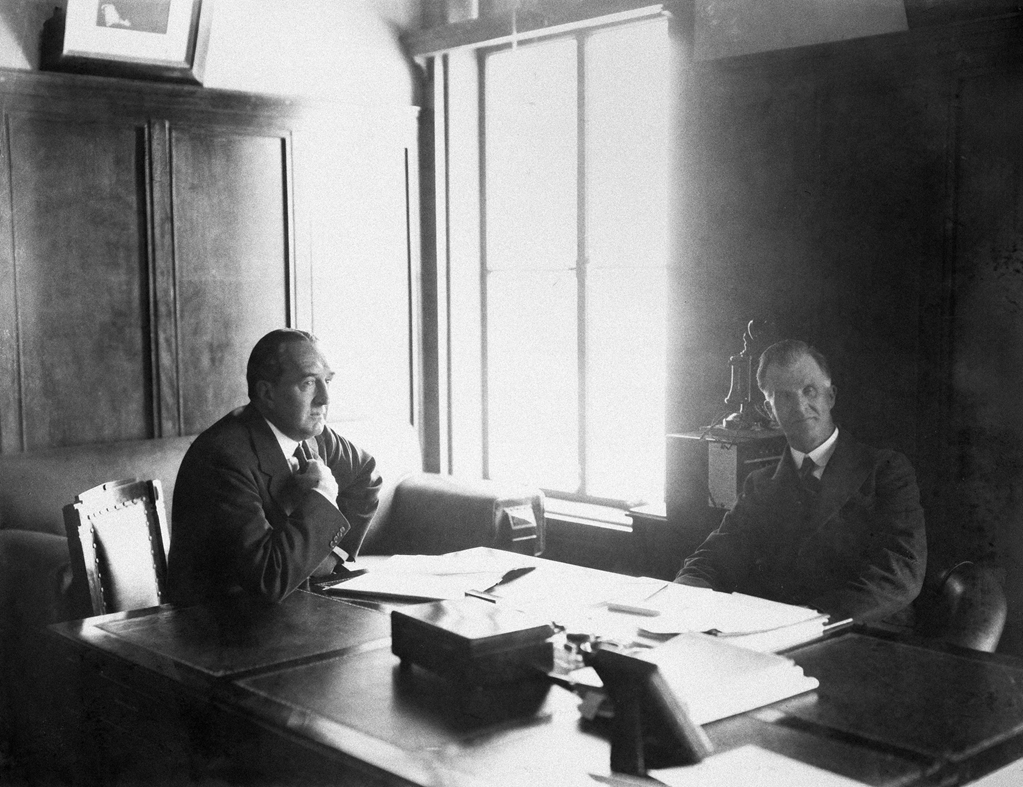 Bruce and Scullin sit at a large wooden desk