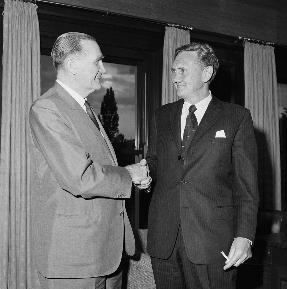 John McEwen shakes John Gorton's hand. Gorton is holding a cigarette.