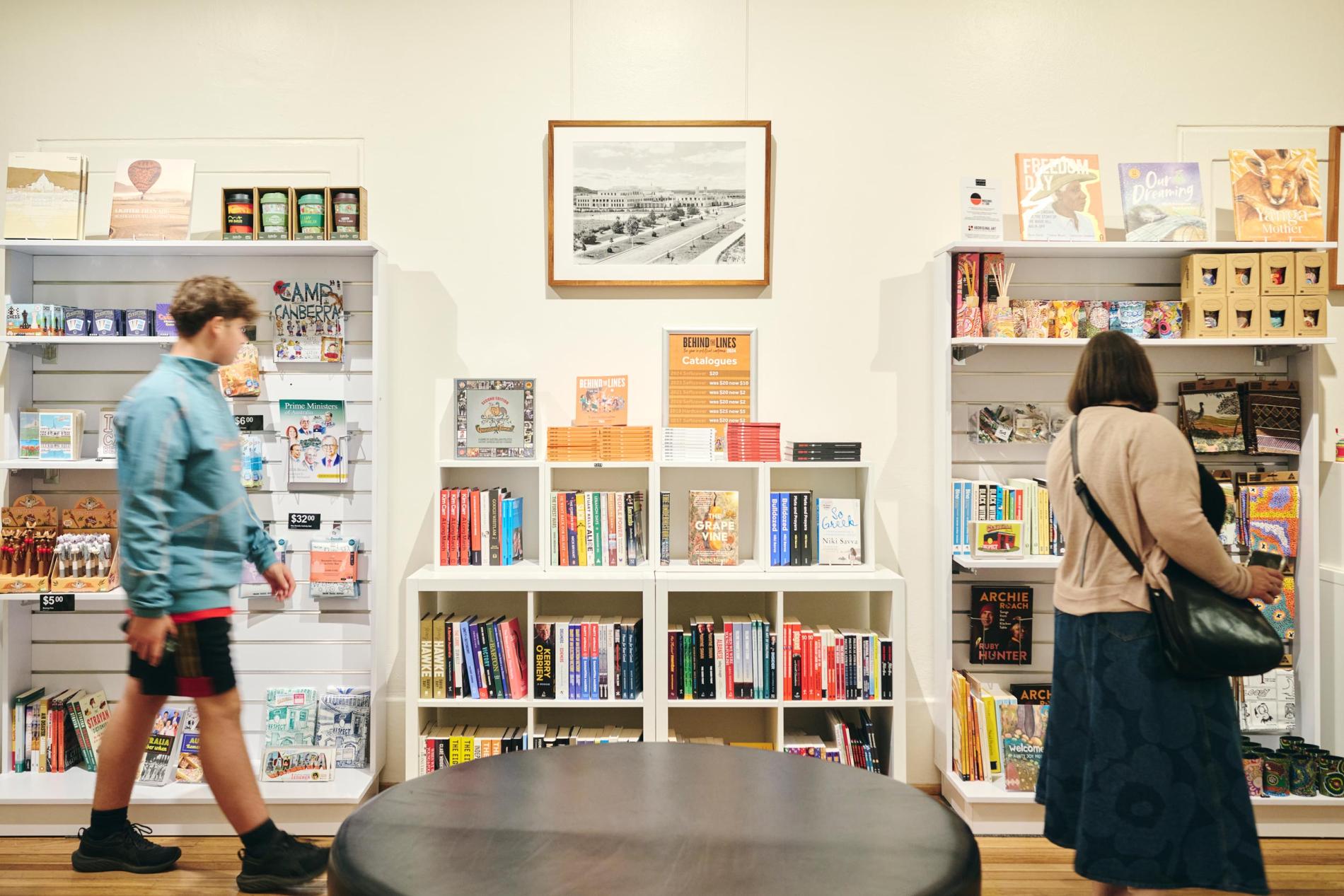 Two people browse books and other shop products on shelves. Two people browse books and other shop products on shelves.