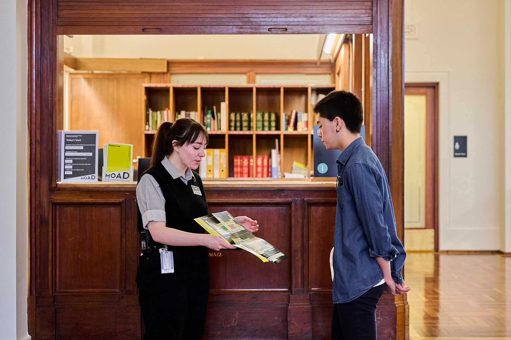 An Old Parliament House museum staff member stands in King's Hall showing a visitor a map.