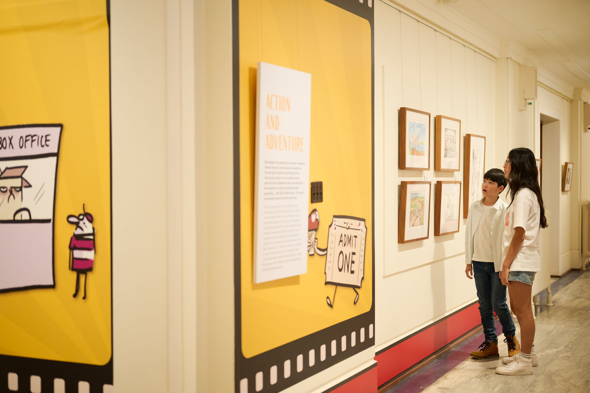Two kids look at a wall of political cartoons in Old Parliament House.