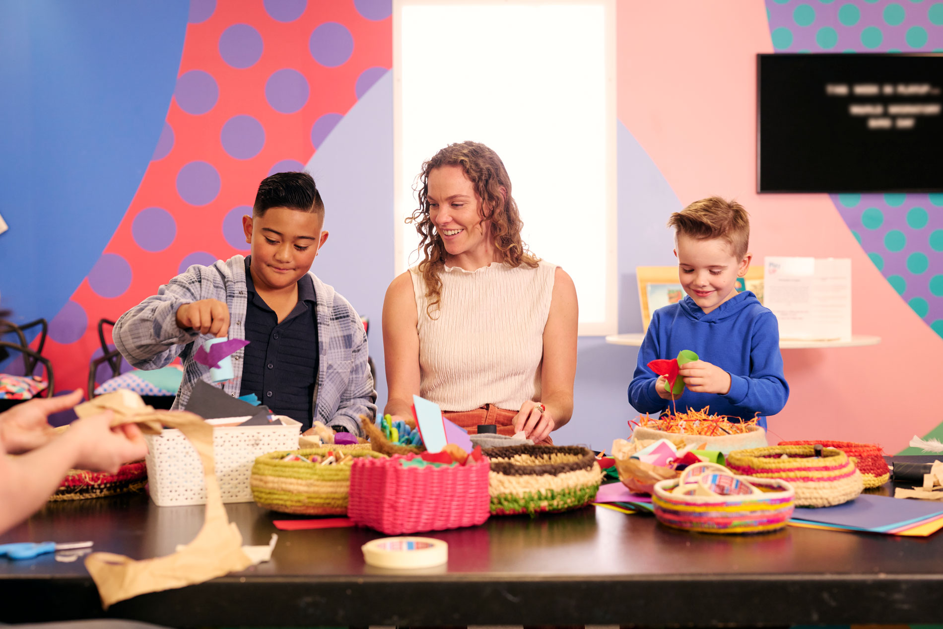 Two kids and a woman craft at a table filled with colourful baskets at Old Parliament House.
