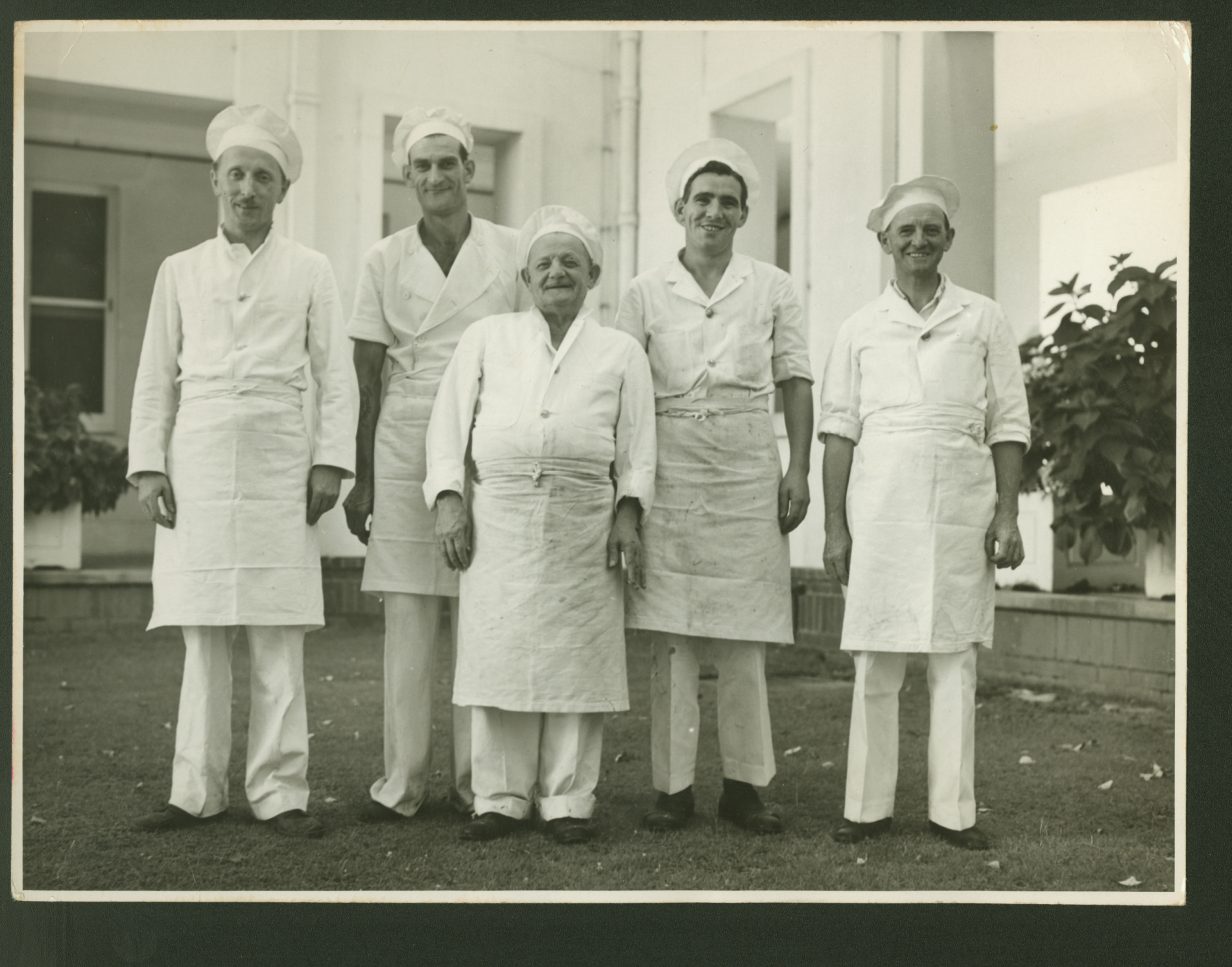 Five cook wearing their uniforms, standing outside in one of the courtyards at Old Parliament House while smiling at the camera.