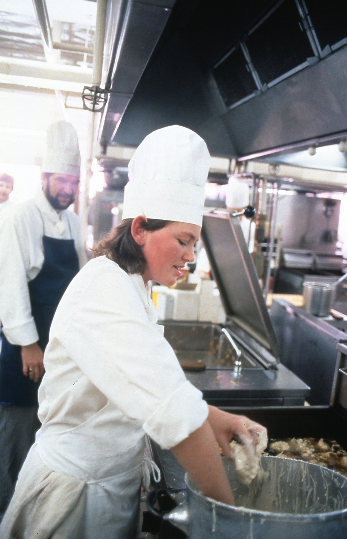 A cook in the kitchen at Old Parliament House putting a meat in batter.