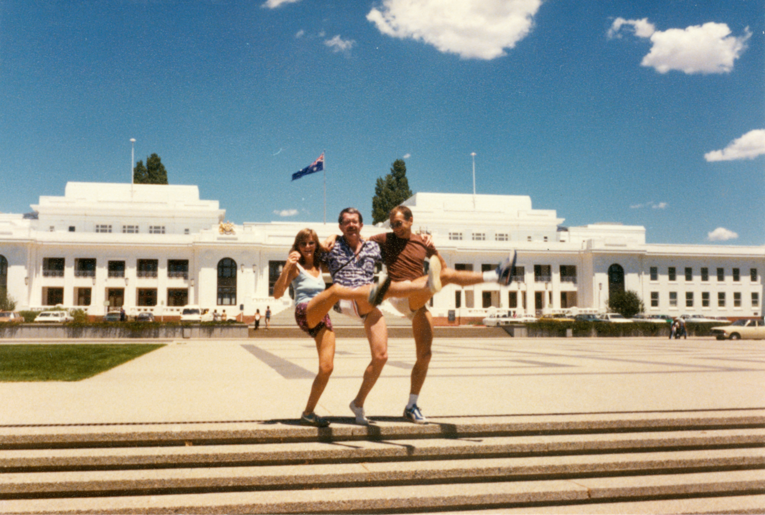 3 people dancing on the front steps of Old Parliament House on a sunny, slightly cloudy day.