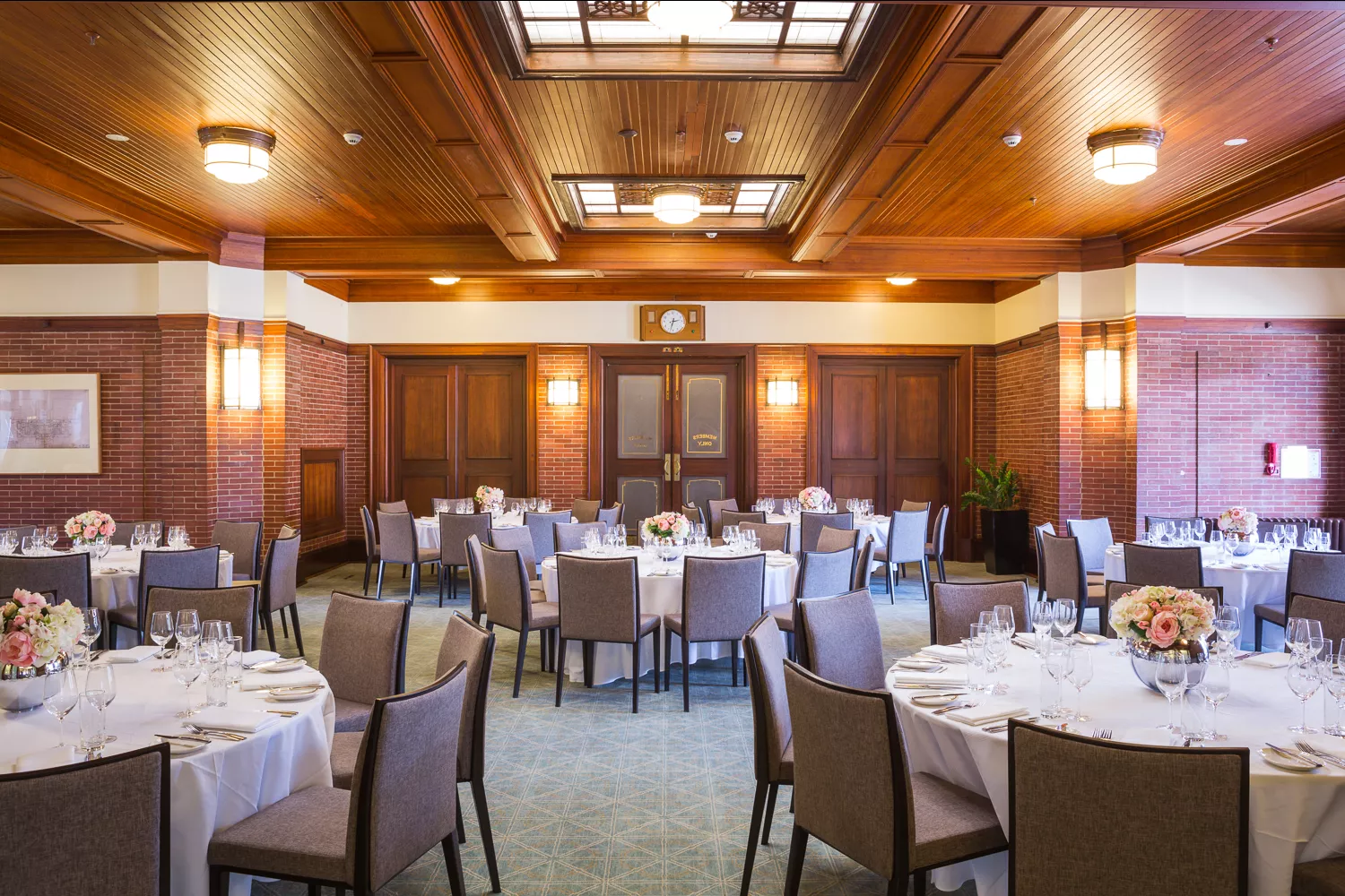 A room with a timber roof and many circular tables covered in white tablecloths. 