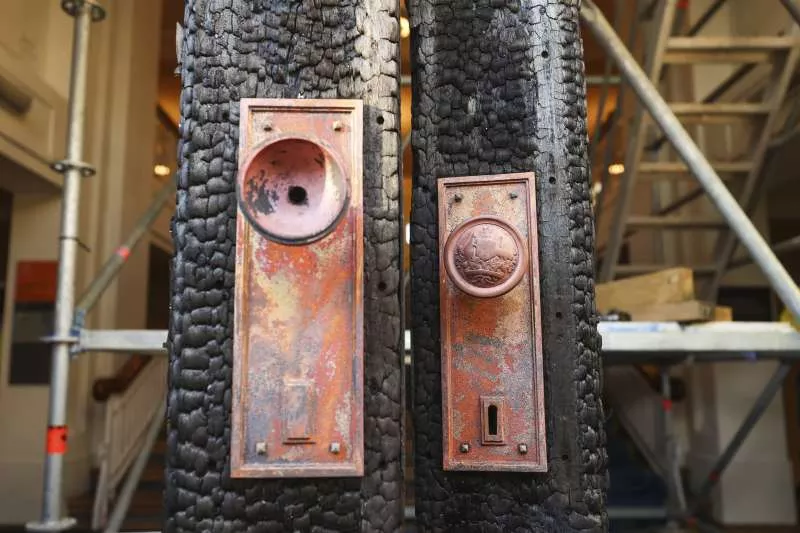 Two sets of brass doorknobs on a burnt and blackened door frame.