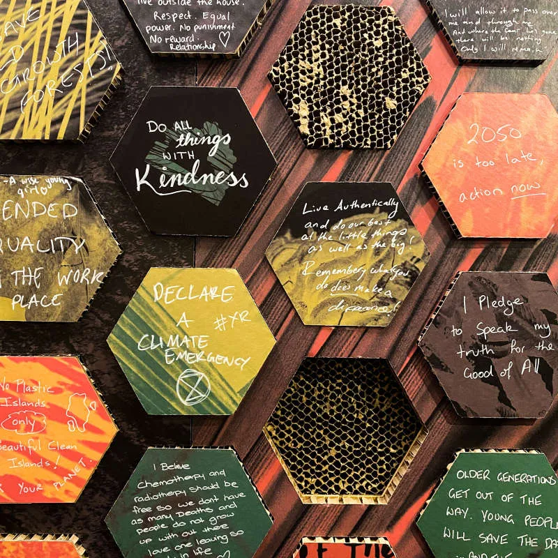 A wall with colourful hexagon tiles in a honeycomb pattern, with ideas and messages hand written in each tile.