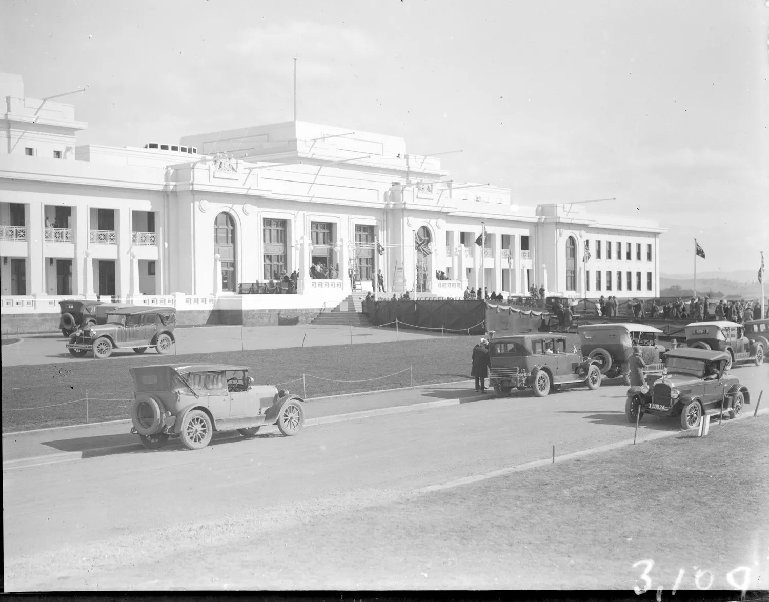 A black and white photo from 1927 of a large white building, Old Parliament House, with cars driving past.