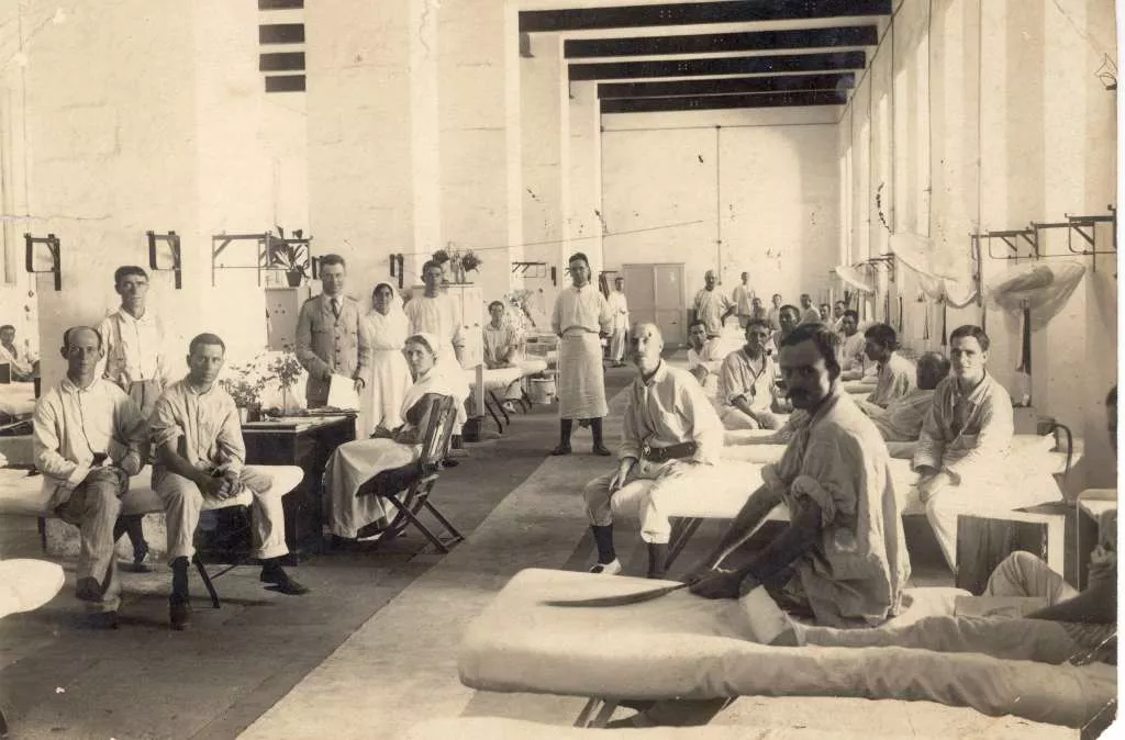 Earle Page (in the suit) standing a field hospital surrounded by medical staff and patients sitting in their beds.