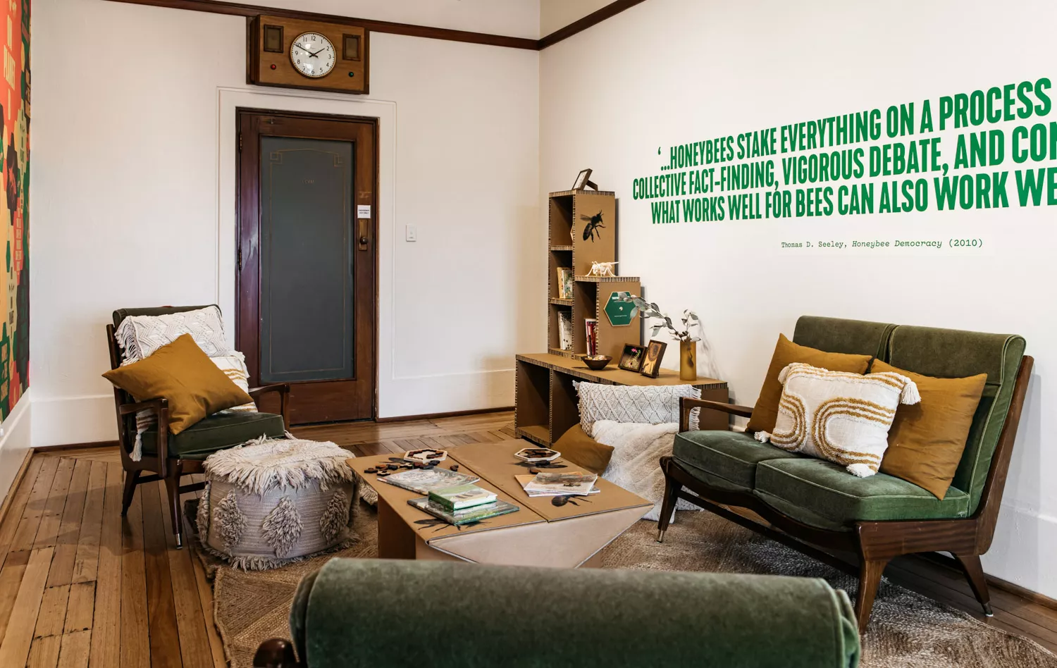 A room with green couches, cushions on the floor and books on the bookshelf. 
