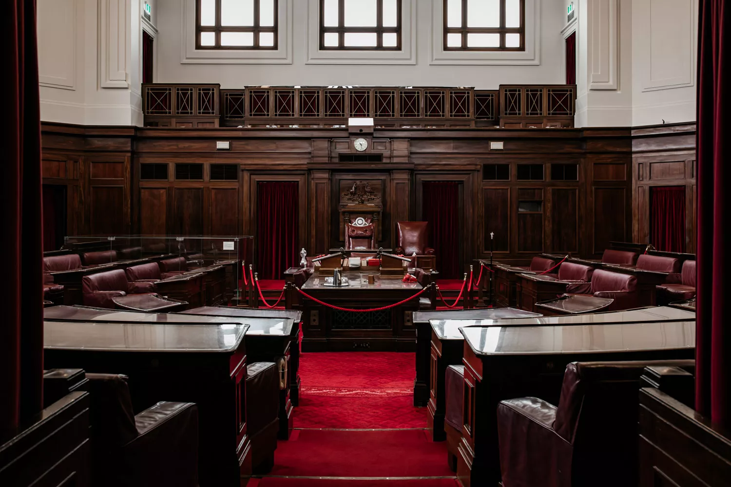 Two small steps with red carpet leading into the Senate Chamber with dark wooden furniture positioned in U-shape around a central table. 