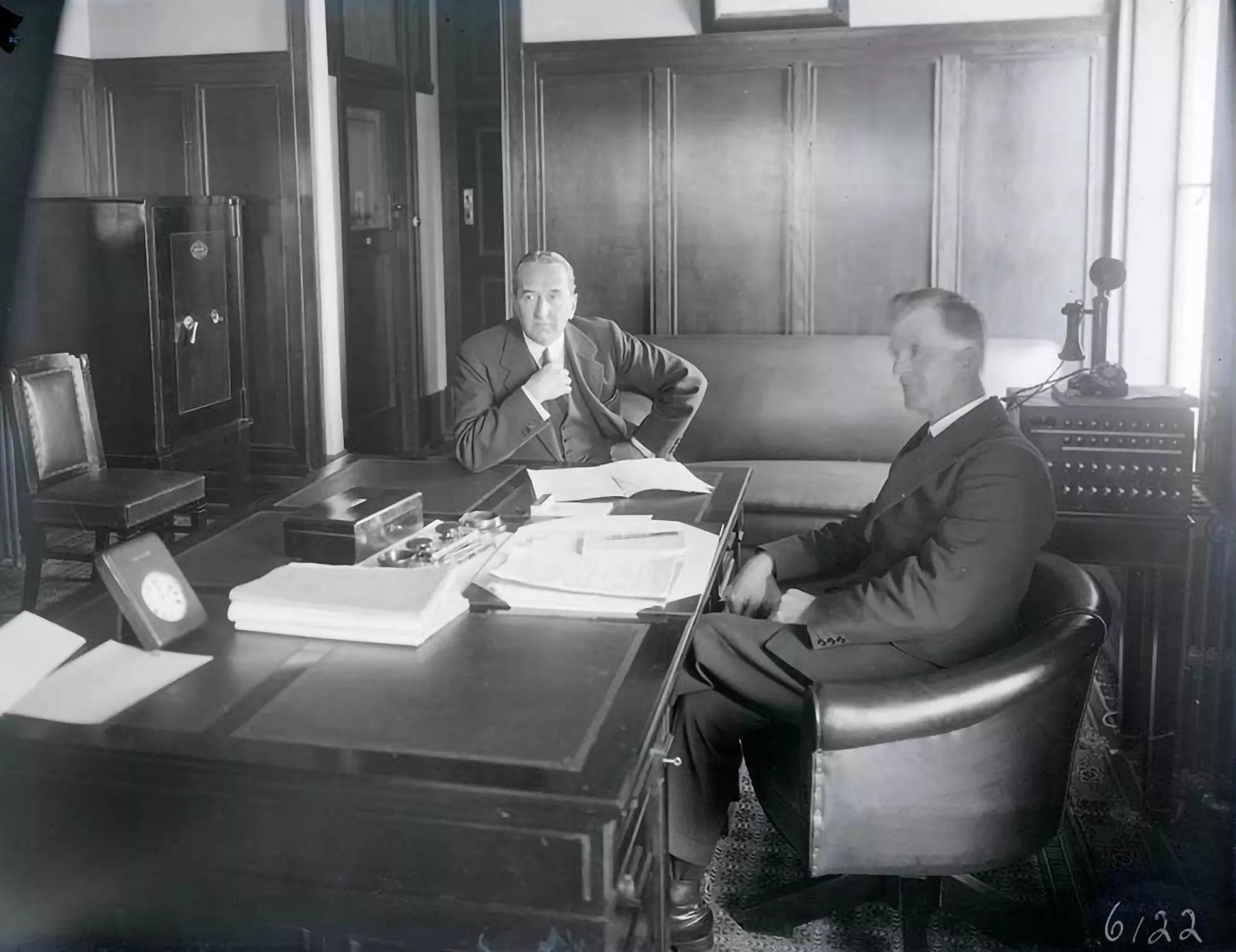 Two men in suits, Stanley Bruce and James Scullin, sit at a large wooden desk.