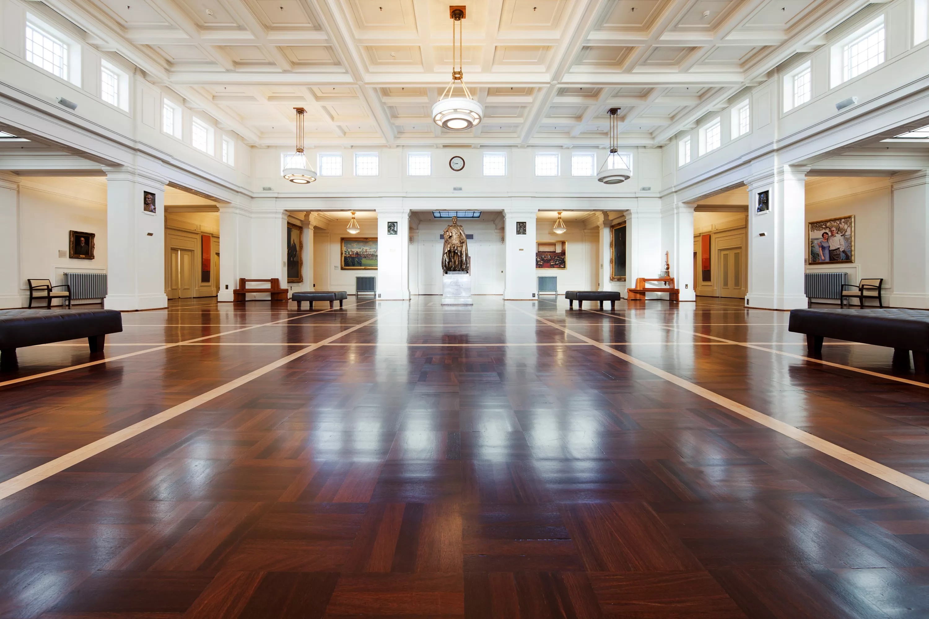 The large central room of Old Parliament House, King's Hall, features timber floors, white ornate ceilings and a statue in the distance. 