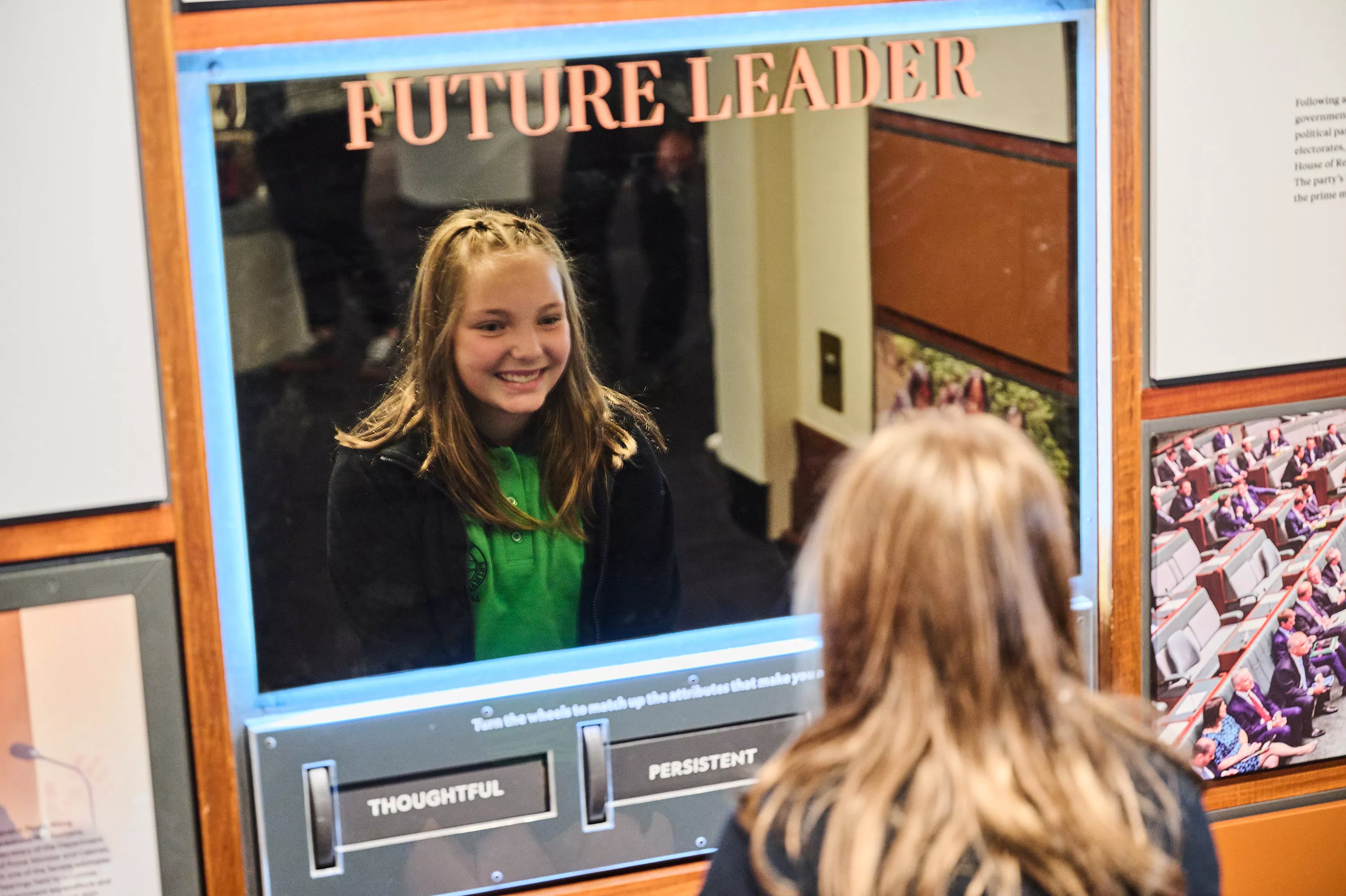 A girl looks in a mirror that has the words 'future leader' on it. 