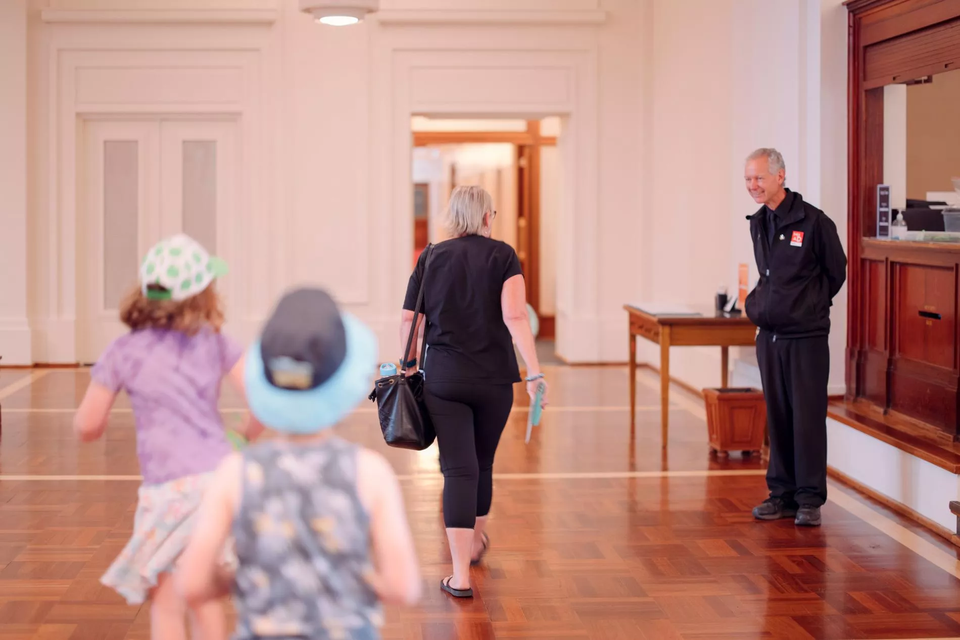 A woman and two children walk towards a museum experience officer dressed in a black uniform with a MoAD badge.