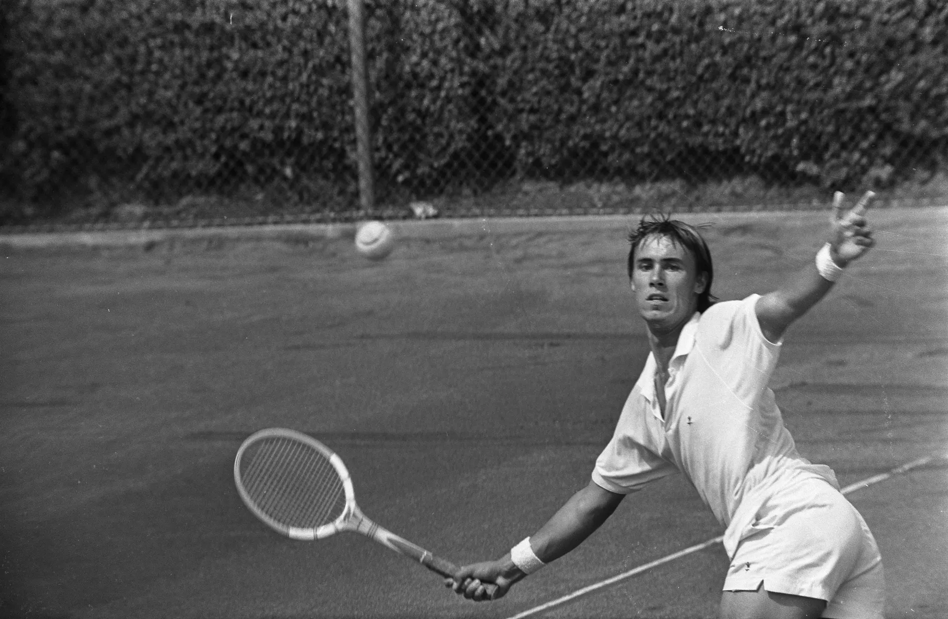 John Alexander wearing a white short sleeved shirt and shorts, playing tennis.