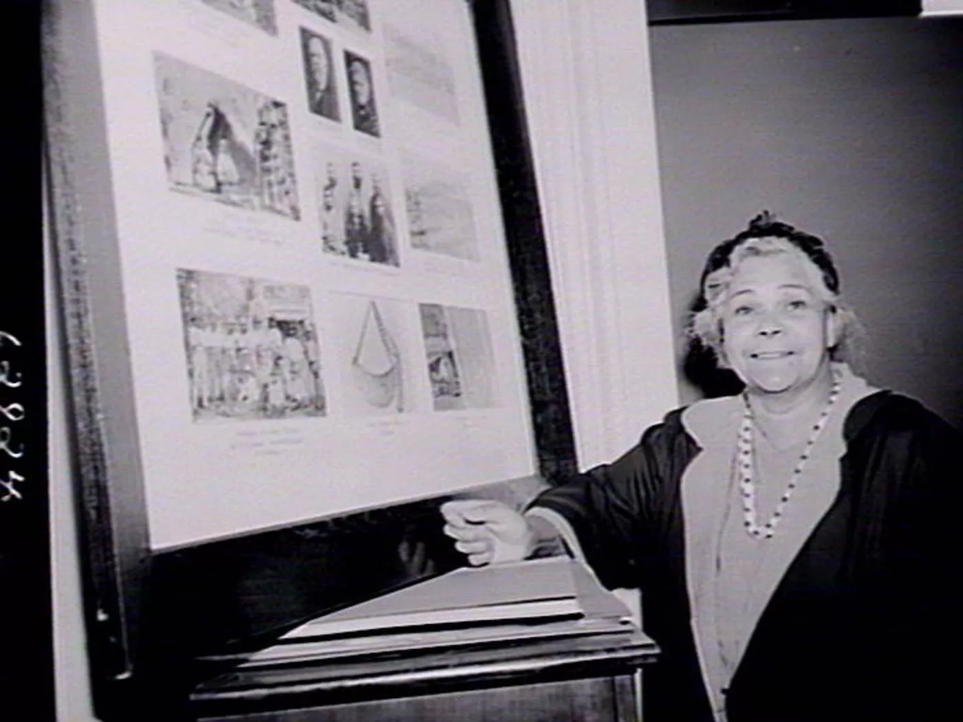 A woman, Margaret Tucker, stands next to a large picture frame filled with images.