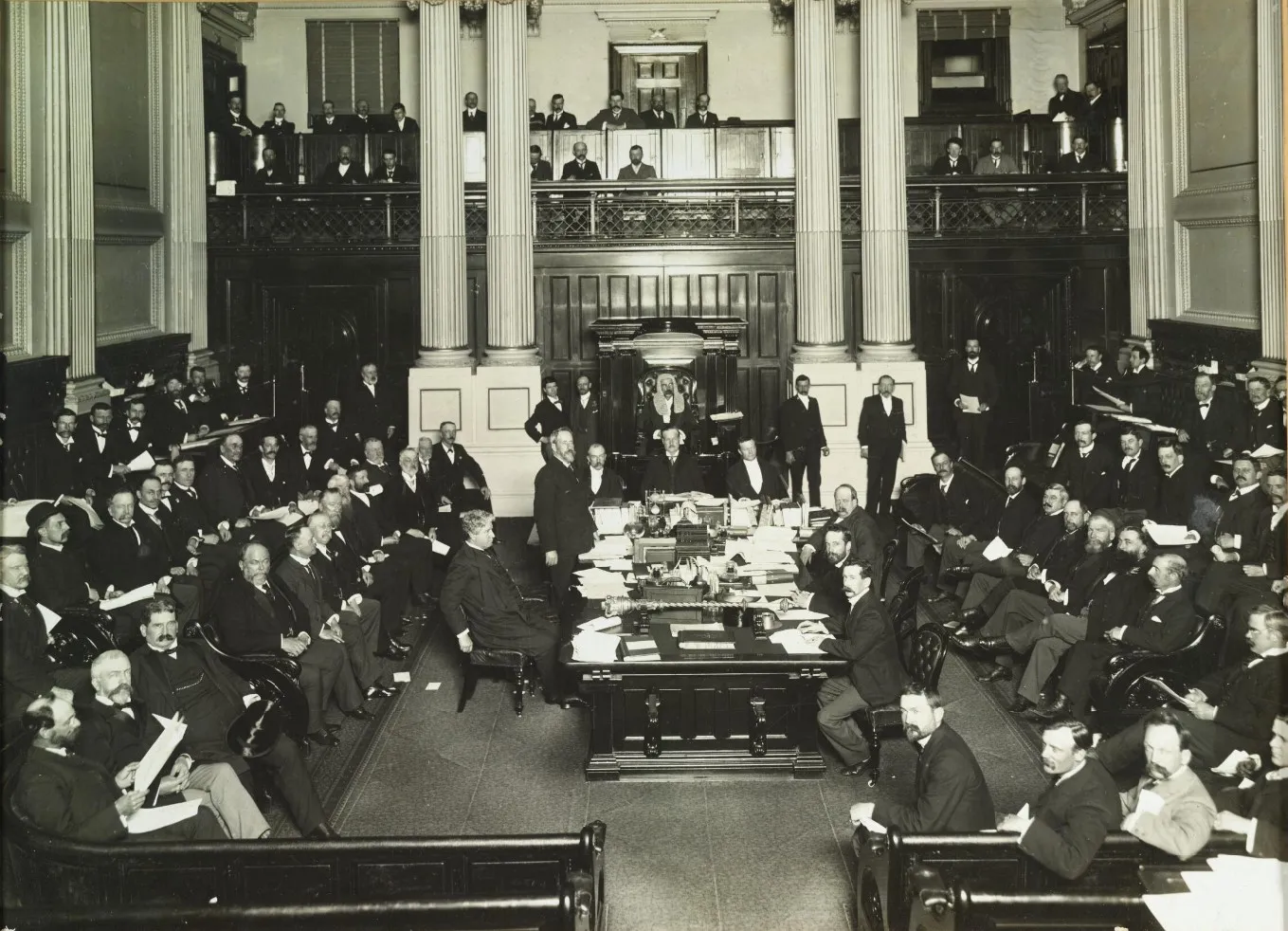 Black and white photo of the Members of the House of Representatives gathered in the Victorian Legislative Assembly chamber in 1901.