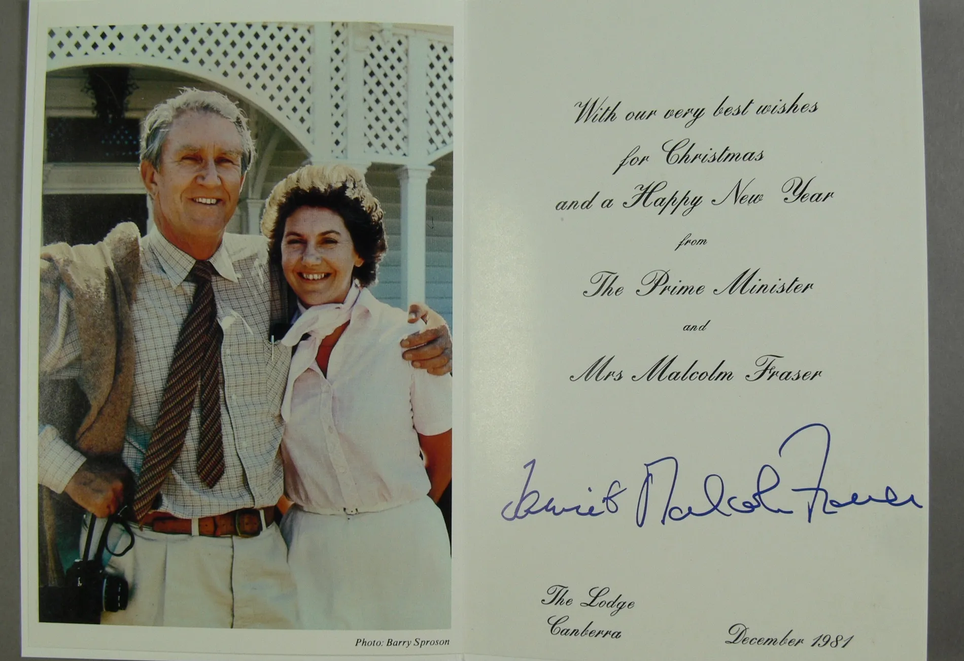 A Christmas card featuring an image of Malcolm Fraser standing with a tweed jacket hanging on his shoulder, and an arm around Tamie Fraser. wearing a pink blouse and white neckscarf.