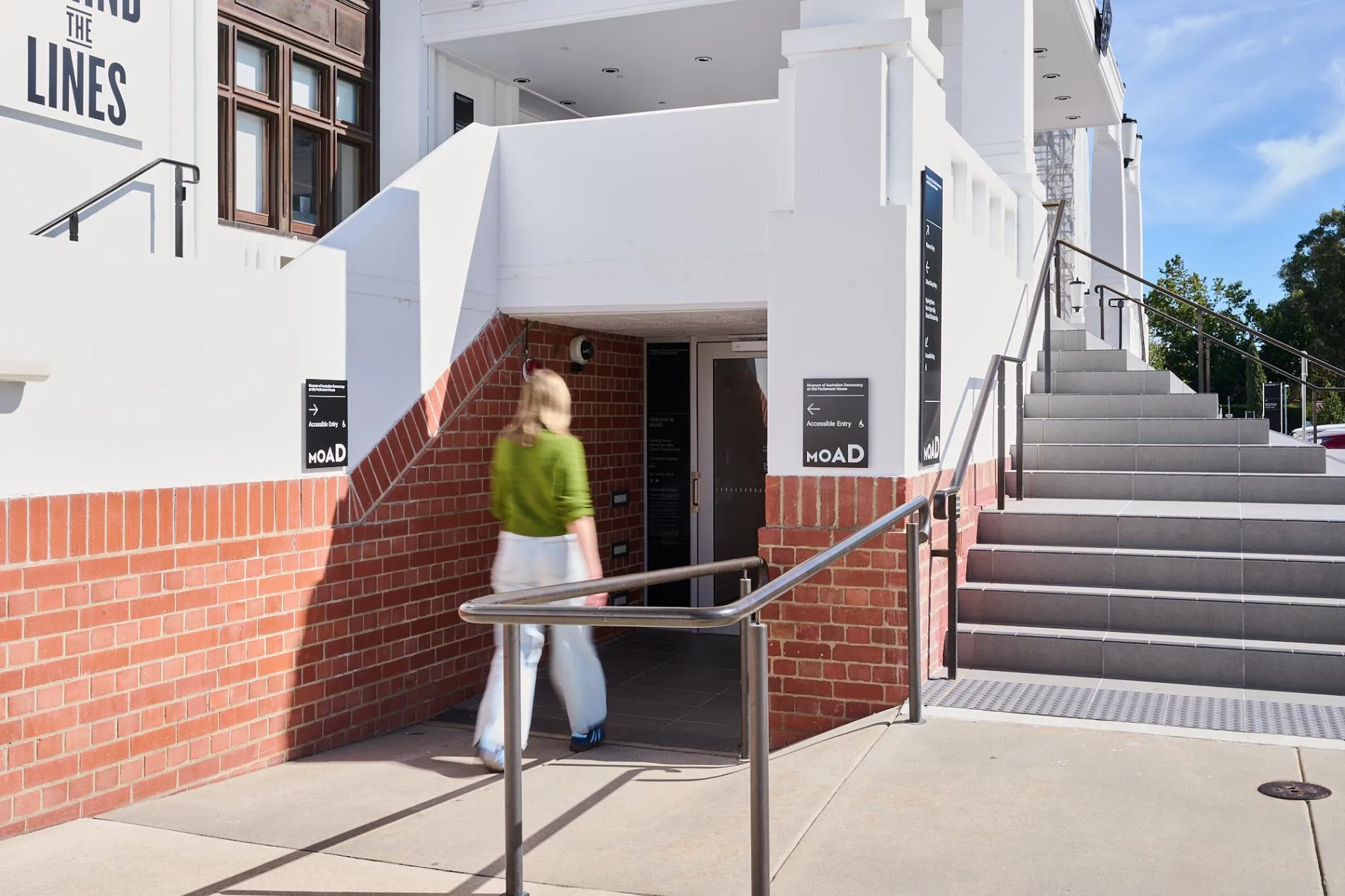 A woman in a green sweater walks into the accessible entry at Old Parliament House.