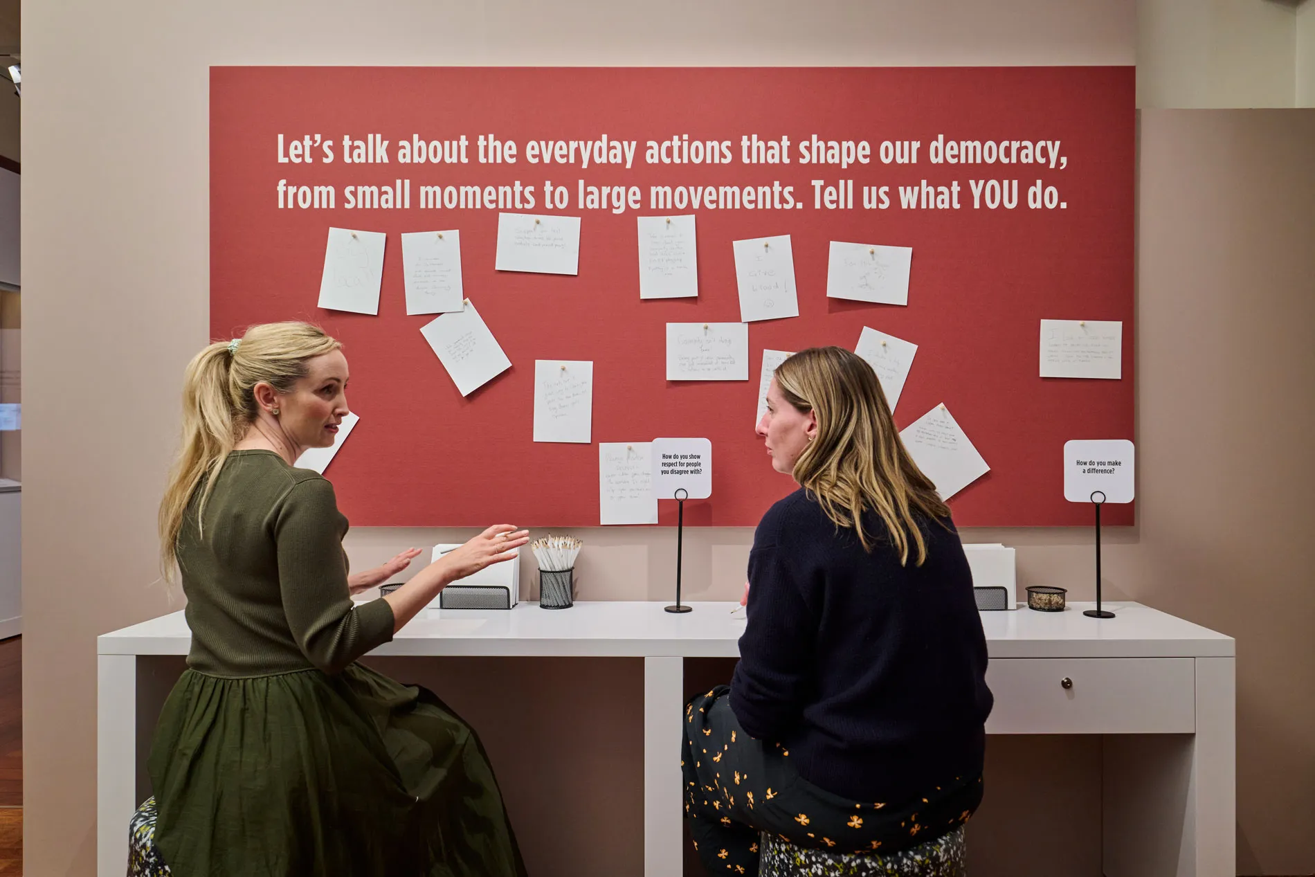 Two people sit in front of a wall of notes in the Democracy Are You In exhibit in Old Parliament House.