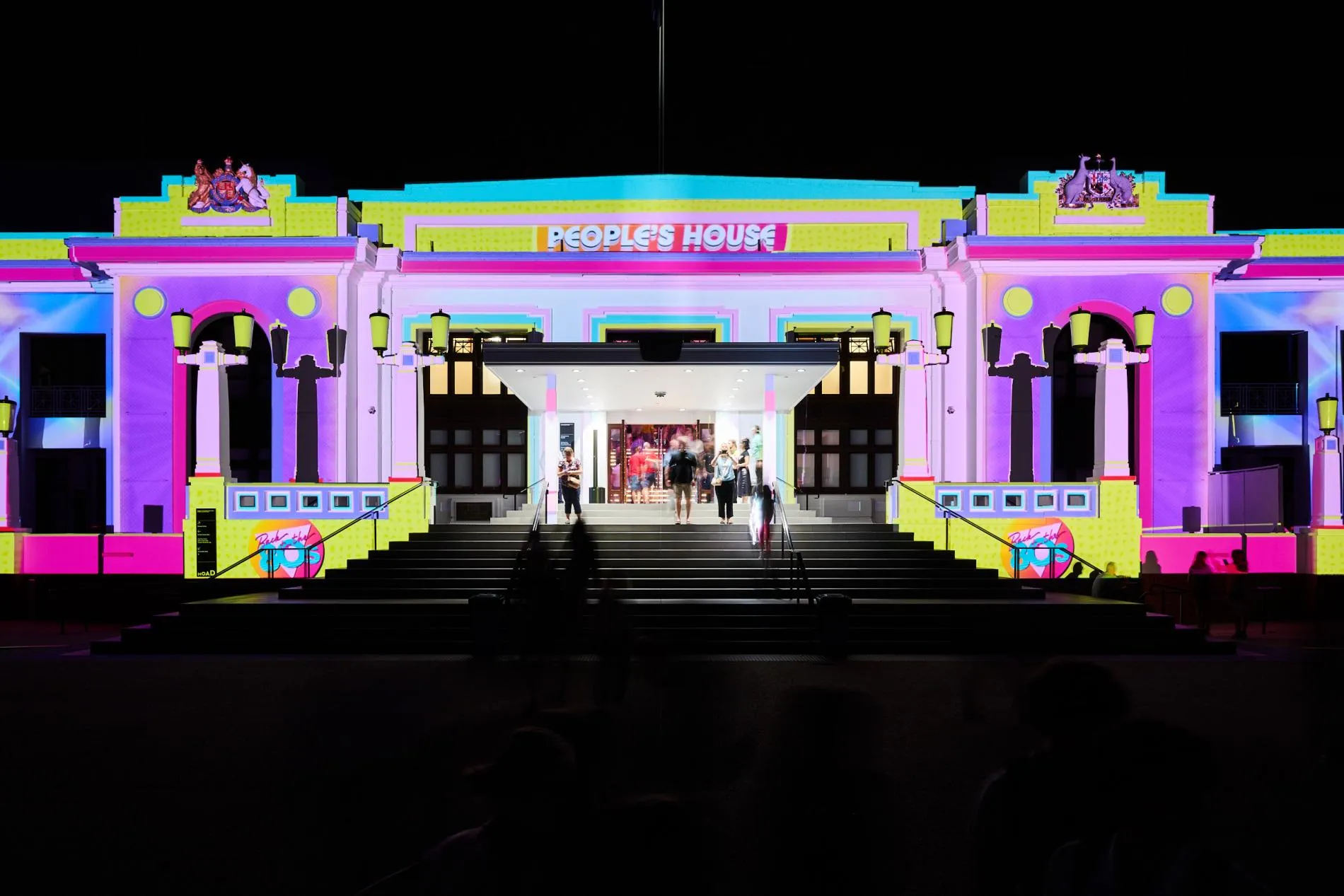 The front of Old Parliament House illuminated in bright neon colours for a light festival.