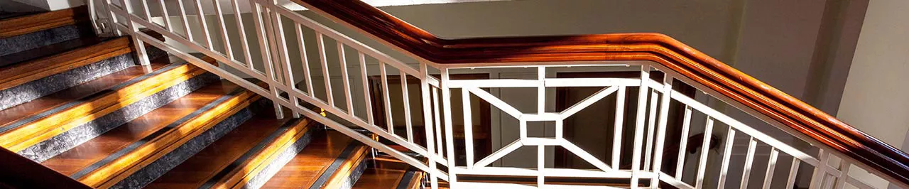 A close up of a timber staircase with dappled light. The railings feature white posts with an art-deco style design.