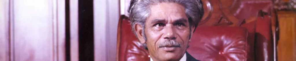 Neville Bonner seated in the Senate chamber, wearing a suit and red tie.