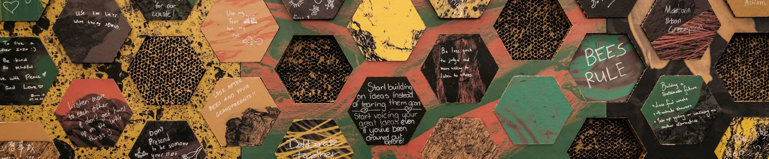 A cardboard installation of a wall with intersecting honeycomb shapes with words written in texta on them with slogans such as 'fight for democracy, love freedom'.