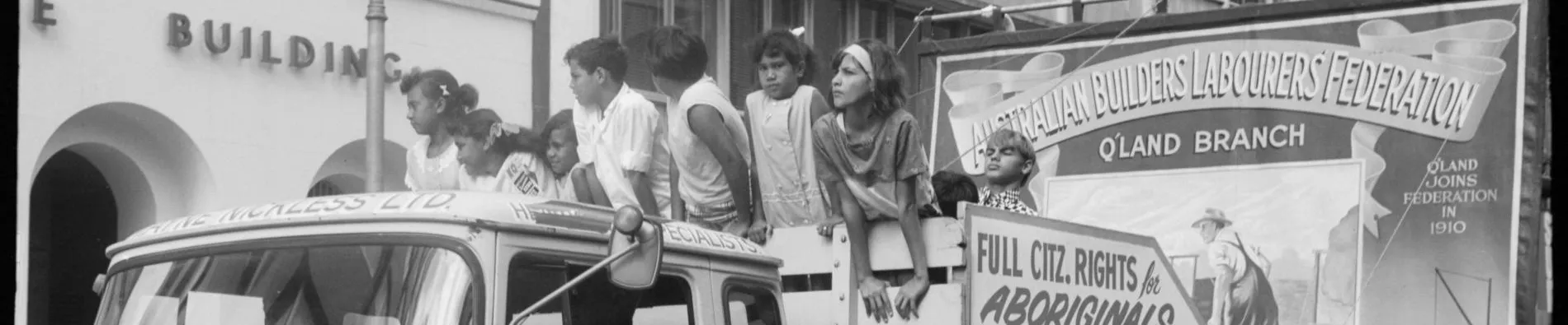 A black and white photo of a car and a float with a group of people standing in front of a sign that reads full citz rights for Aboriginals.