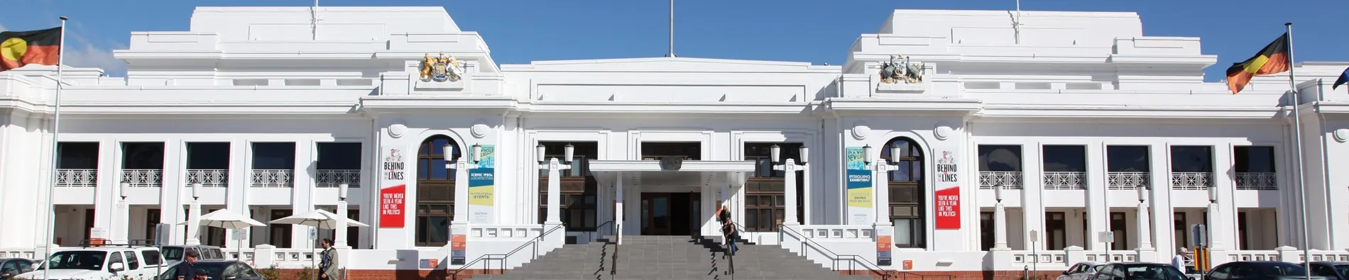 Front of Old Parliament House, flying the Australian flag and two Aboriginal flags, with people standing at the front stairs.