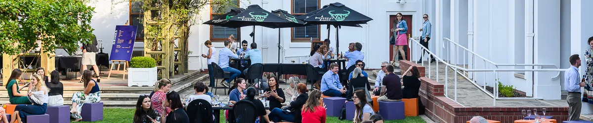 People sit at tables and on stools in the Old Parliament House courtyard having drinks.