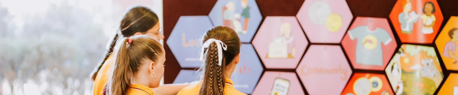 Three students in uniform looking at the hexagonal pieces of Democracy in a Box on the wall.