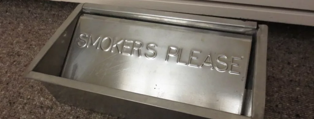 A metal floor ashtray with the inscription 'SMOKERS PLEASE'.