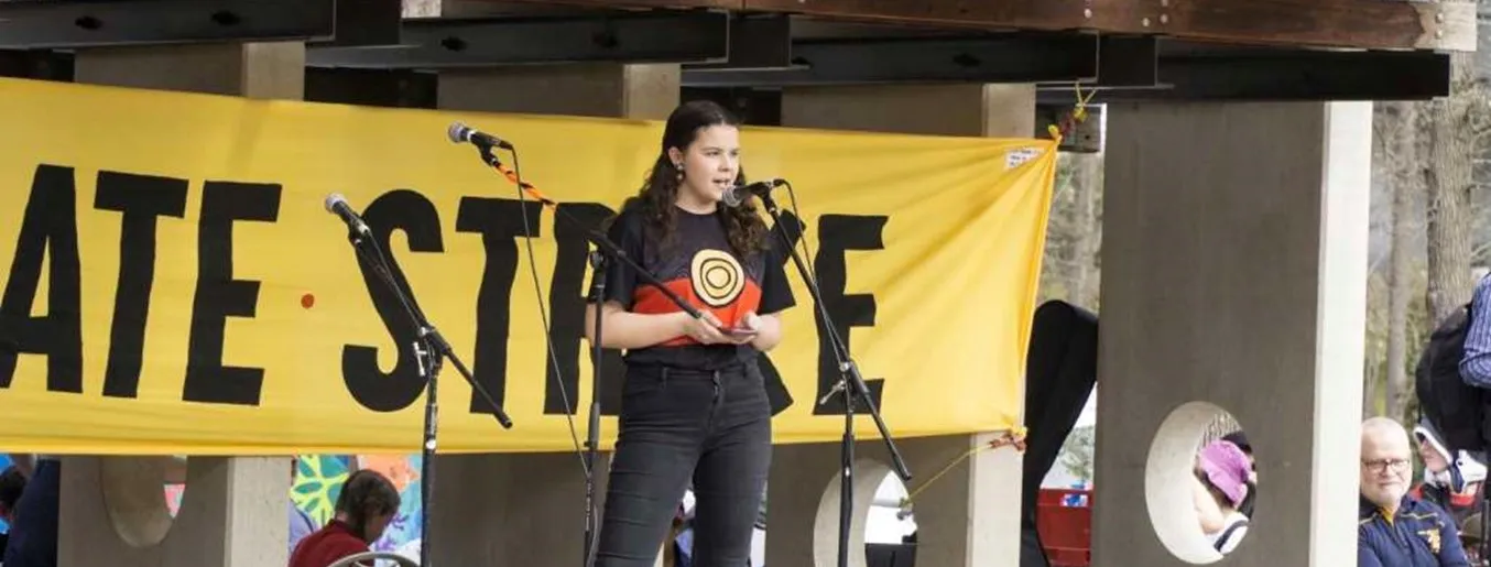 Dhani Gilbert speaks into a microphone, on stage, for a school strike for climate change protest