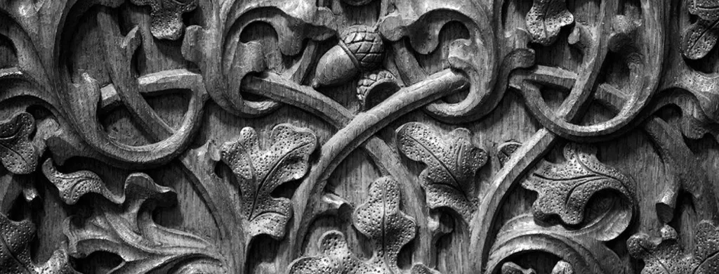 Black and white close-up photo of oak leaf and acorn shaped carvings into a wooden panel.