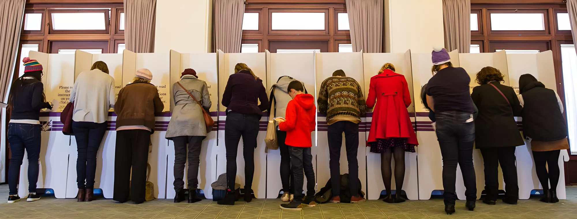 A line of twelve people, each standing at a cardboard voting booth.