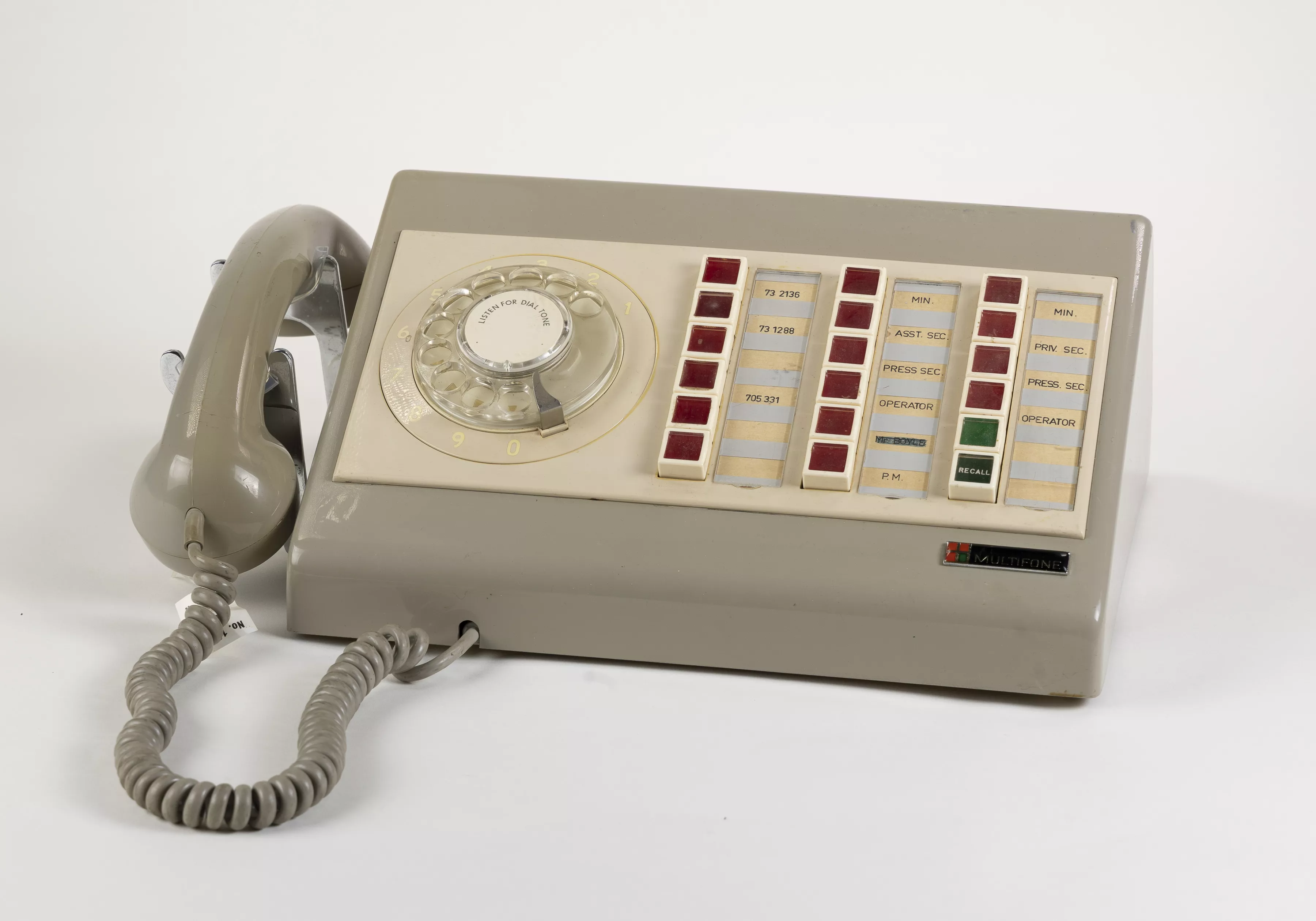 A light taupe plastic Multifone phone with 16 red buttons, 2 green buttons and a manual hand dial. The receiver sits on the side with a curly rubber cord.