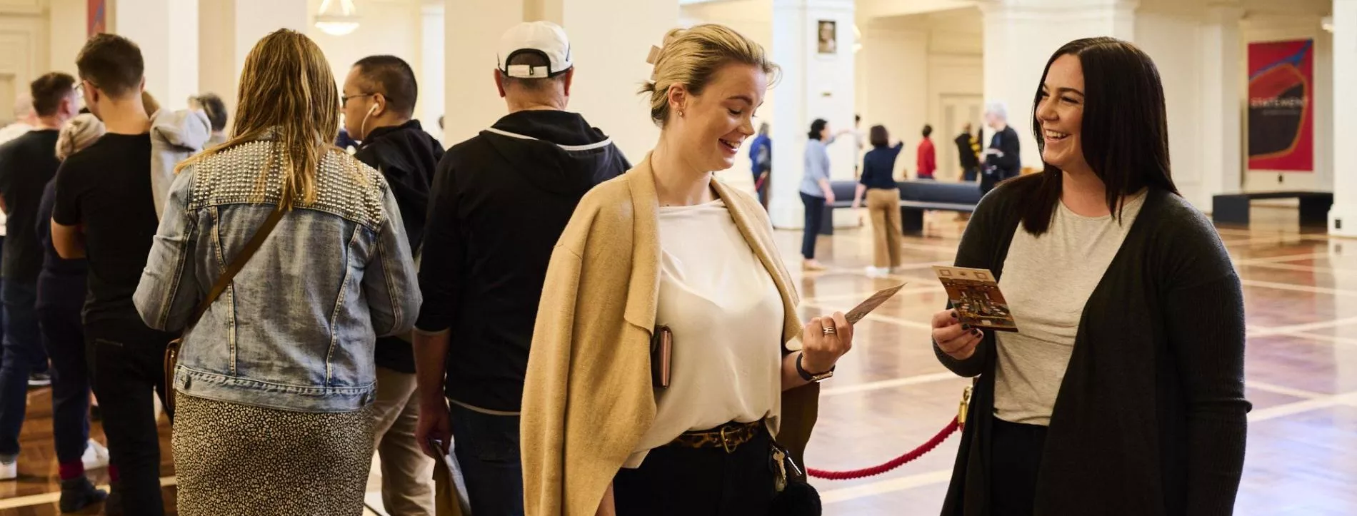 Two women talk to each other in a queue in King's Hall. 