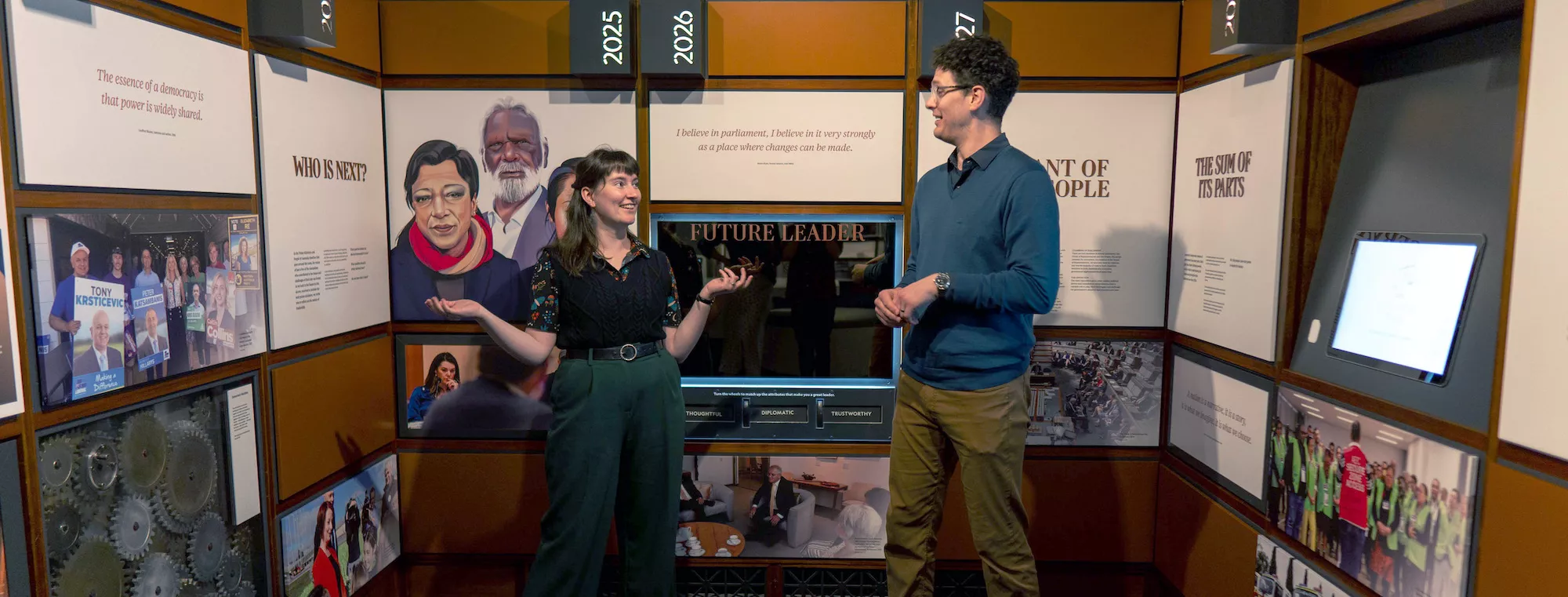 Photograph of two learning presenters standing in front of a wall with a mirror that says "future leaders"